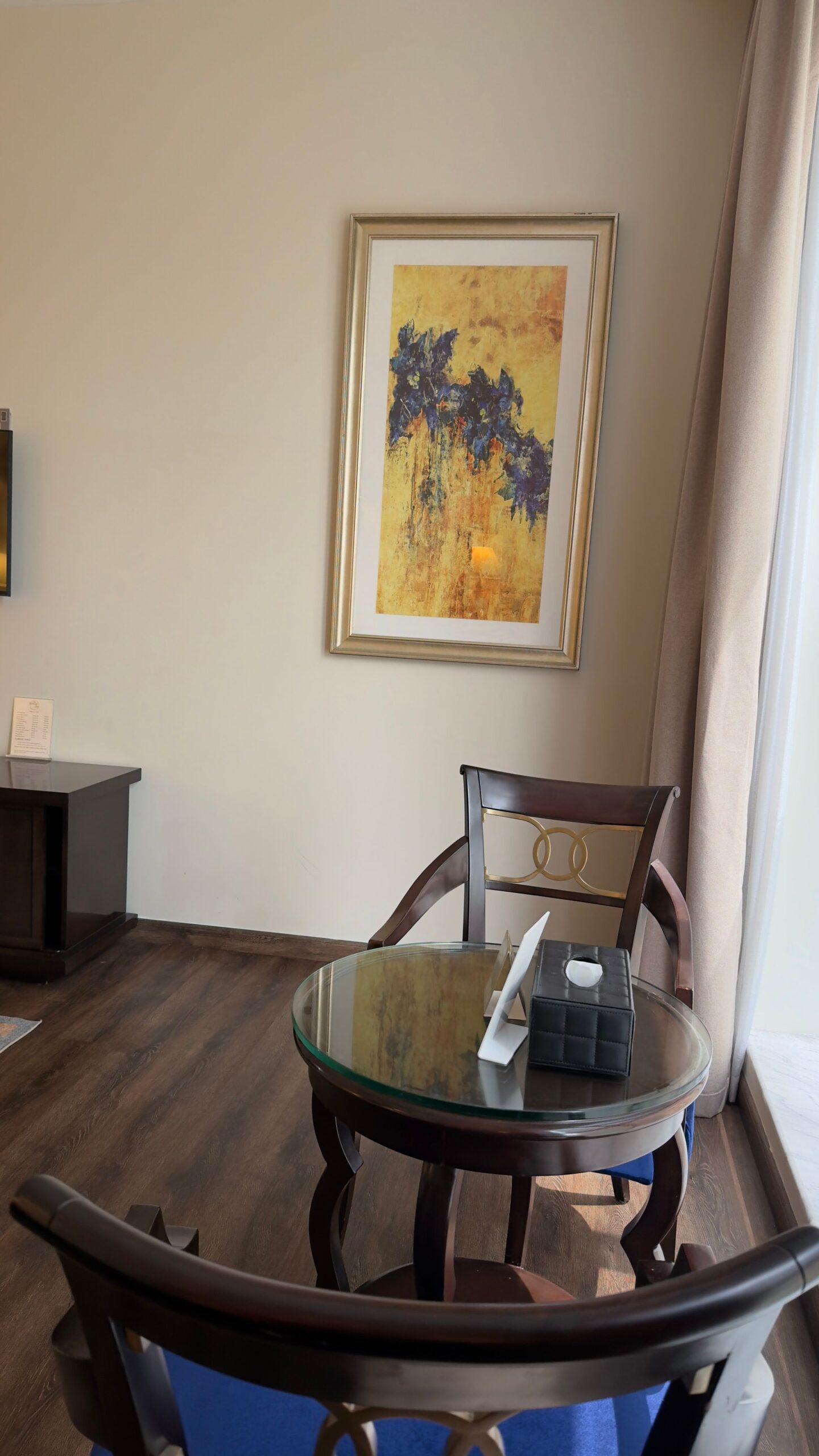 Elegant hotel room seating area with a round glass table and two chairs.
